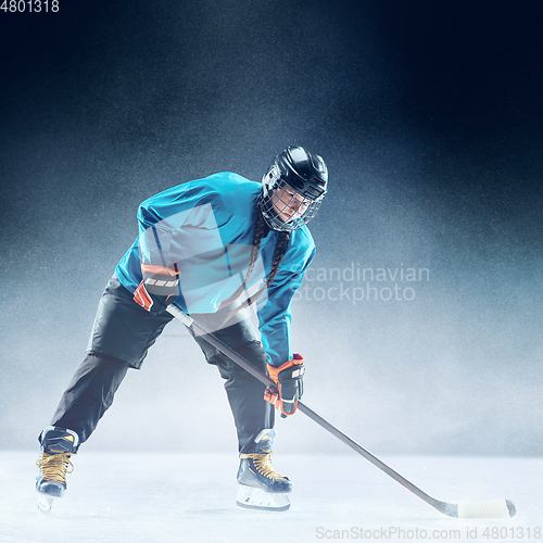 Image of Young female hockey player with the stick on ice court and blue background