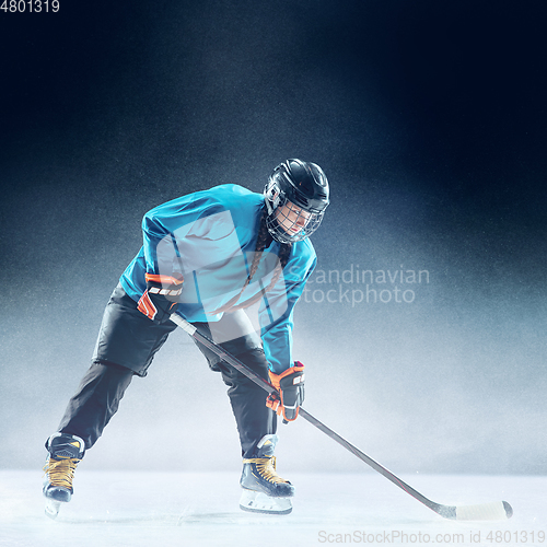 Image of Young female hockey player with the stick on ice court and blue background