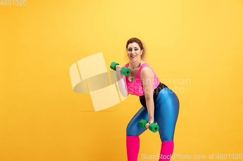 Image of Young caucasian plus size female model\'s training on yellow background