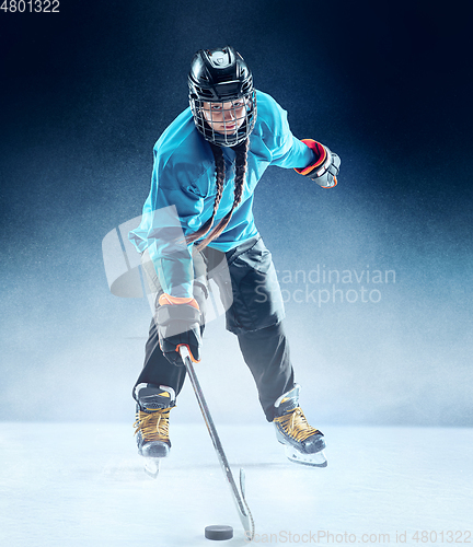 Image of Young female hockey player with the stick on ice court and blue background