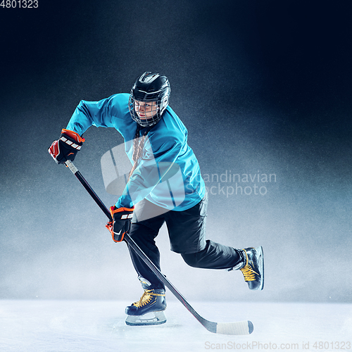 Image of Young female hockey player with the stick on ice court and blue background