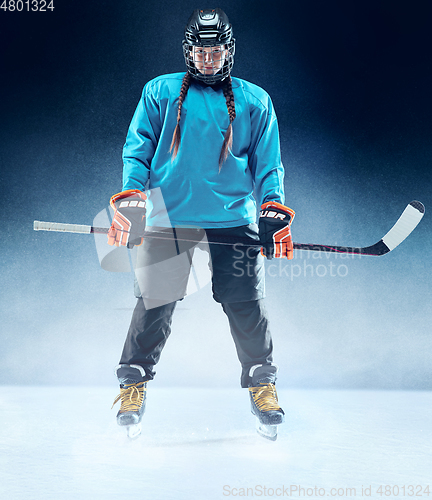 Image of Young female hockey player with the stick on ice court and blue background