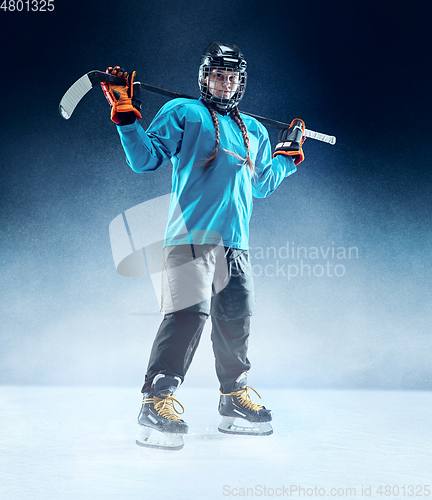 Image of Young female hockey player with the stick on ice court and blue background