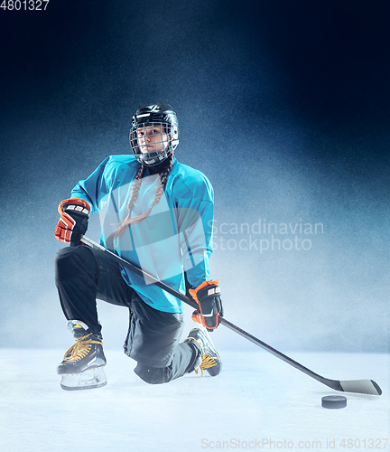 Image of Young female hockey player with the stick on ice court and blue background