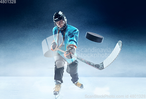 Image of Young female hockey player with the stick on ice court and blue background