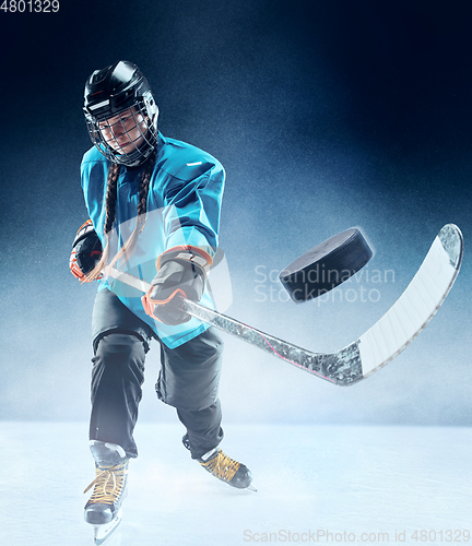 Image of Young female hockey player with the stick on ice court and blue background