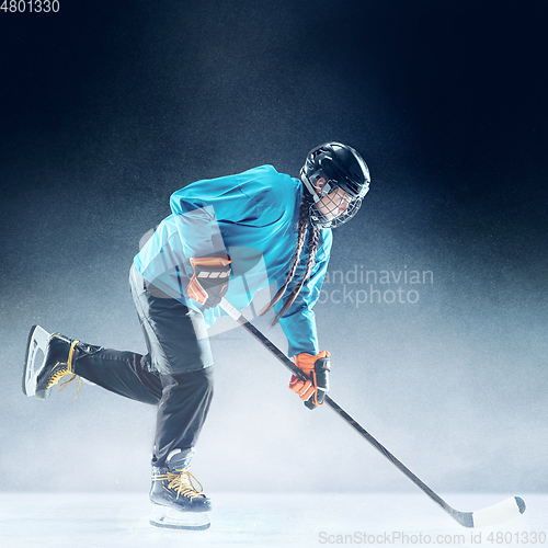 Image of Young female hockey player with the stick on ice court and blue background