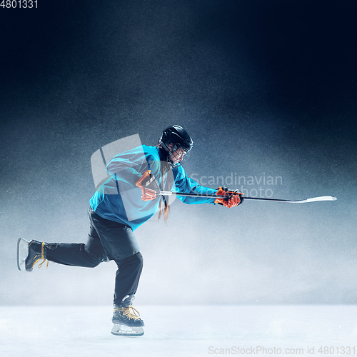 Image of Young female hockey player with the stick on ice court and blue background