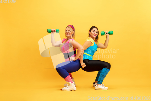 Image of Young caucasian plus size female models training on yellow background