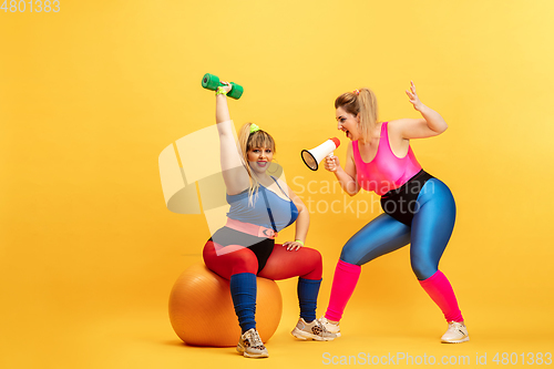 Image of Young caucasian plus size female models training on yellow background