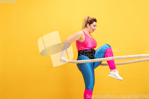 Image of Young caucasian plus size female model\'s training on yellow background