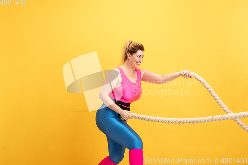 Image of Young caucasian plus size female model\'s training on yellow background