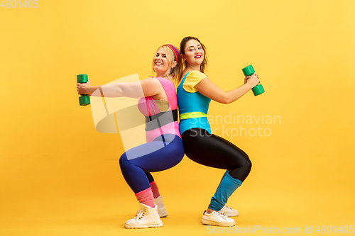 Image of Young caucasian plus size female models training on yellow background