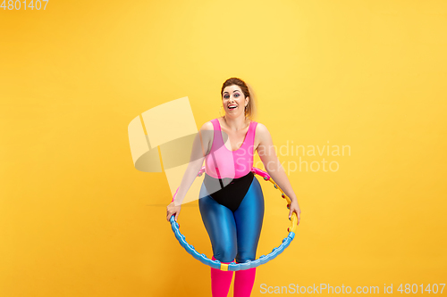 Image of Young caucasian plus size female model\'s training on yellow background