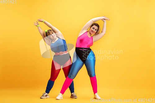 Image of Young caucasian plus size female models training on yellow background
