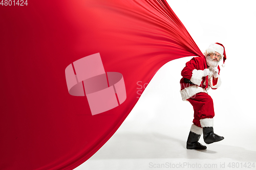 Image of Santa Claus pulling huge bag full of christmas presents isolated on white background