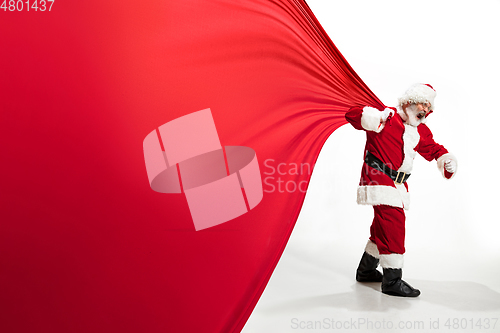 Image of Santa Claus pulling huge bag full of christmas presents isolated on white background