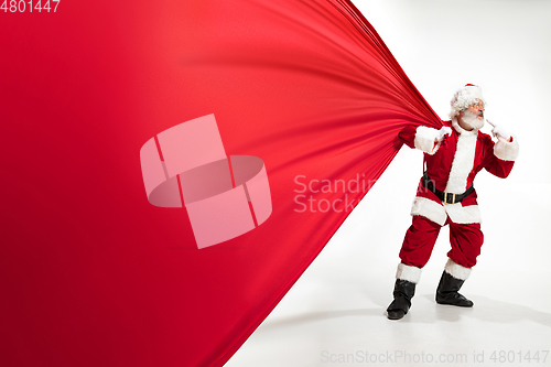 Image of Santa Claus pulling huge bag full of christmas presents isolated on white background