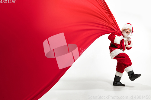 Image of Santa Claus pulling huge bag full of christmas presents isolated on white background