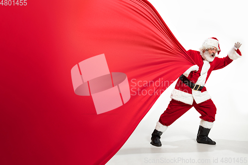 Image of Santa Claus pulling huge bag full of christmas presents isolated on white background