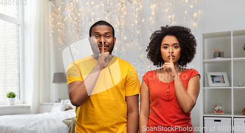 Image of happy african american couple making hush gesture