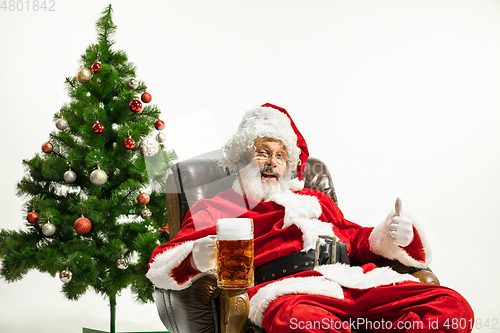 Image of Santa Claus drinking beer near Christmas tree, congratulating of
