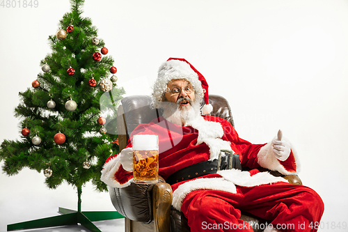 Image of Santa Claus drinking beer near Christmas tree, congratulating of