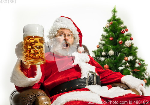 Image of Santa Claus drinking beer near Christmas tree, congratulating of