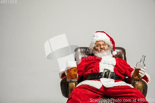 Image of Santa Claus drinking beer sitting on armchair, congratulating of New Year 2020