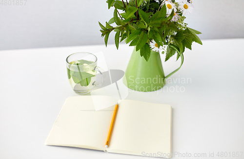 Image of herbal tea, notebook and flowers in jug on table