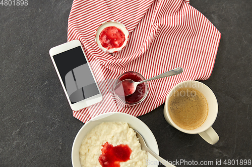 Image of porridge with jam, spoon, coffee and phone