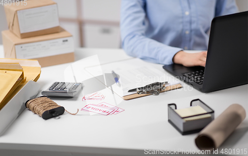 Image of woman with laptop and clipboard at post office