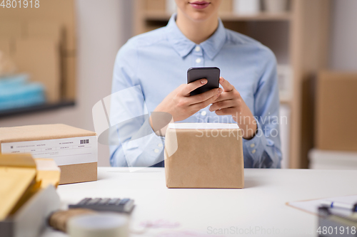 Image of woman with smartphone and parcels at post office