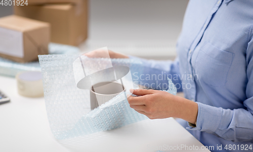 Image of woman packing mug to parcel box at post office