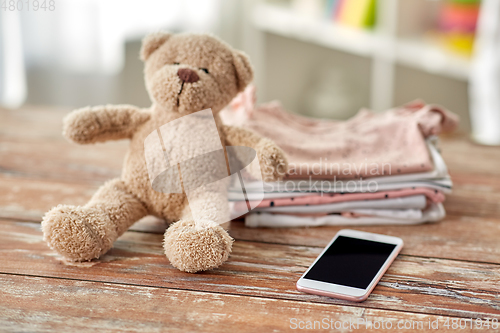 Image of baby clothes, teddy bear toy and smartphone