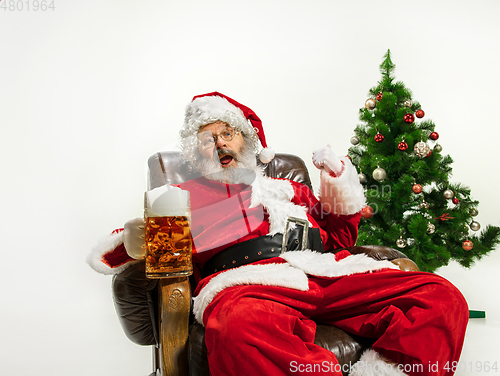 Image of Santa Claus drinking beer near Christmas tree, congratulating of