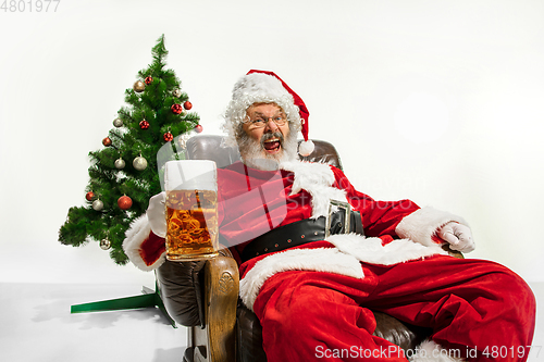 Image of Santa Claus drinking beer near Christmas tree, congratulating of