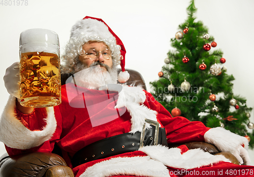 Image of Santa Claus drinking beer near Christmas tree, congratulating of