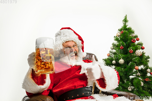 Image of Santa Claus drinking beer near Christmas tree, congratulating of