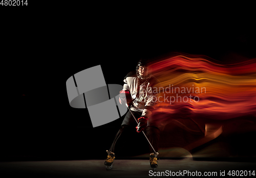 Image of Young female hockey player with the stick on black background in neon light