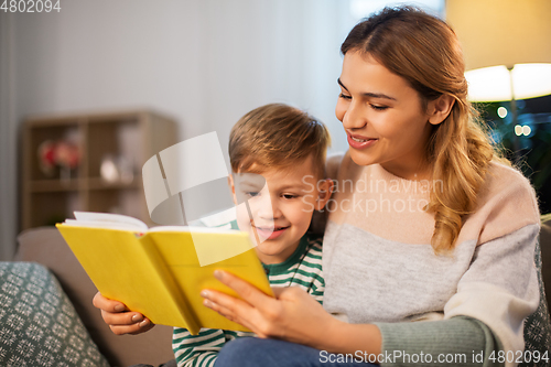 Image of happy mother and son reading book sofa at home