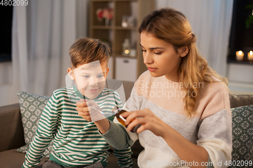 Image of mother giving medication or cough syrup to ill son