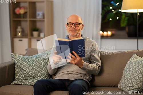 Image of happy bald senior man on sofa reading book at home