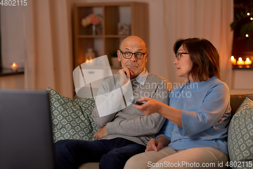 Image of senior couple watching tv at home in evening