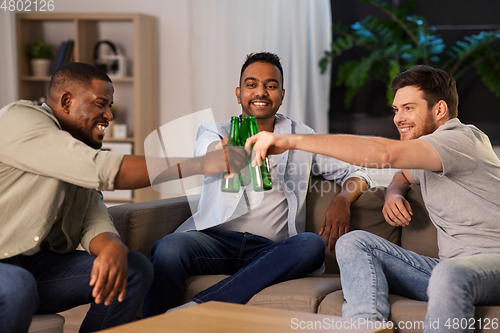 Image of happy male friends drinking beer at home at night