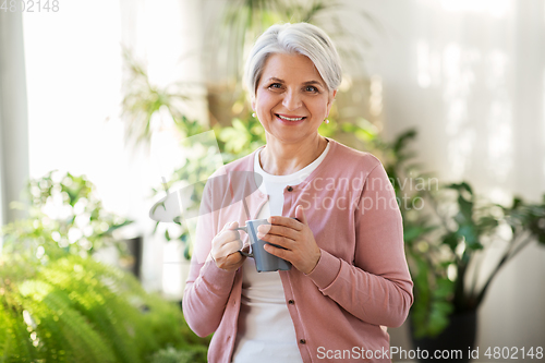 Image of happy senior woman with cup of tea at home
