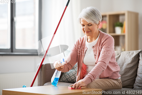 Image of senior woman with detergent cleaning table at home