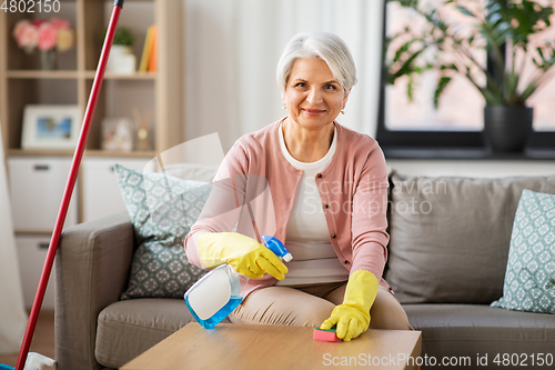 Image of senior woman with detergent cleaning table at home