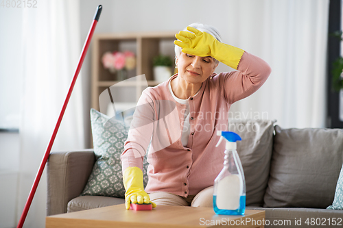 Image of tired senior woman cleaning table at home