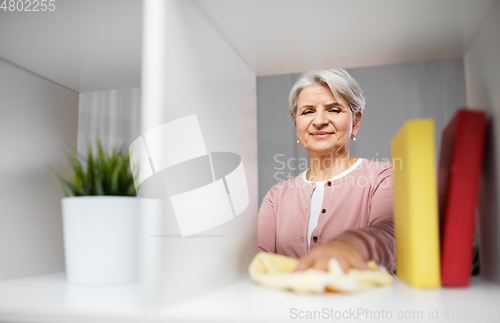 Image of happy senior woman with cloth dusting rack at home